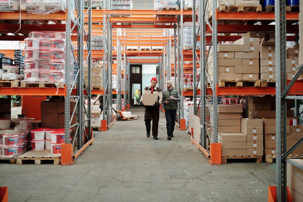 Workers moving stock between pallet racking in a distribution warehouse